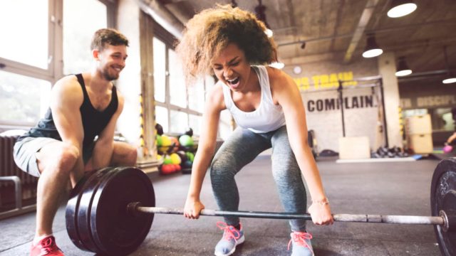 Young woman with training partner preparing to lift barbell in gym