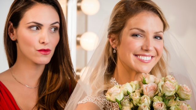 Suspicious bridesmaid standing behind smiling bride
