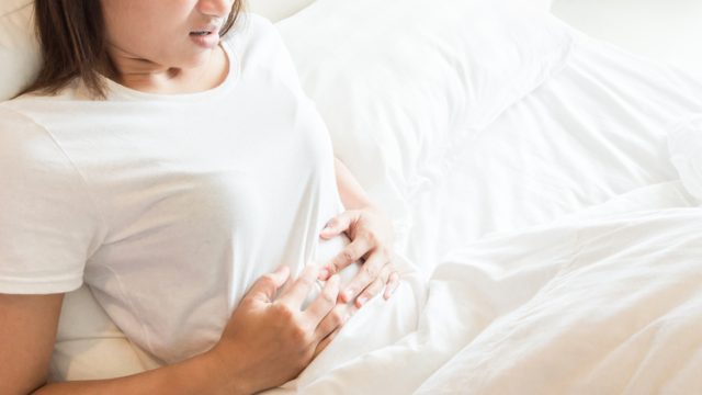 Woman in pain holding her abdomen, lying in bed