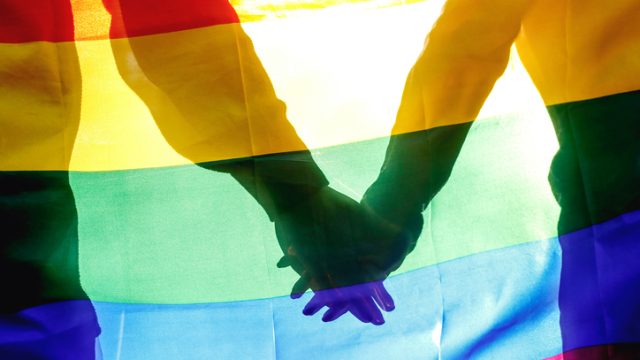 Two people holding hands near Pride flag