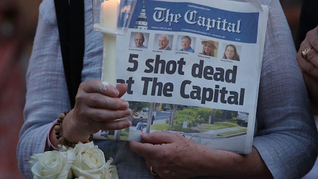 Woman holding up a newspaper at Capital Gazette shooting vigil