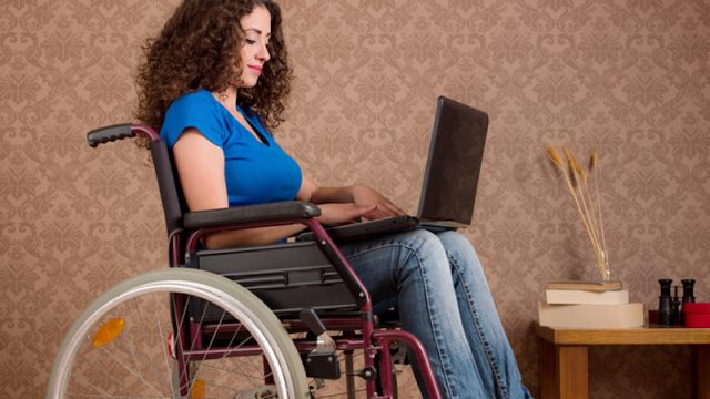Disabled young woman sitting in wheelchair using laptop