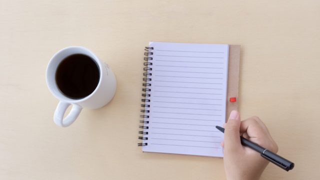 Person writing list next to coffee mug