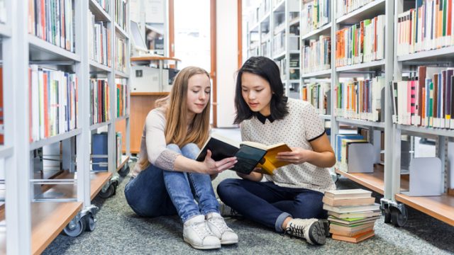 Two young women reading books together