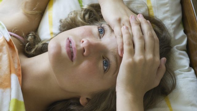Young woman lying on bed with hands clasped on forehead, looking up in thought