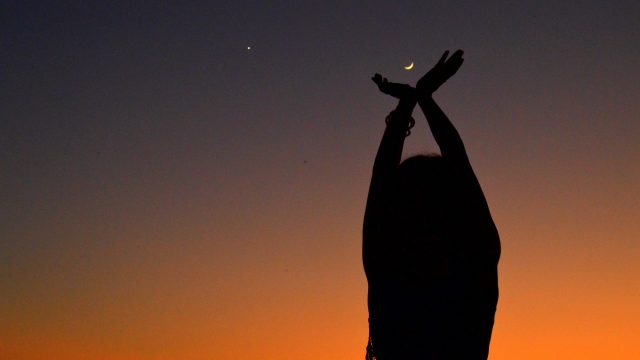 woman against orange sky reaching for new moon