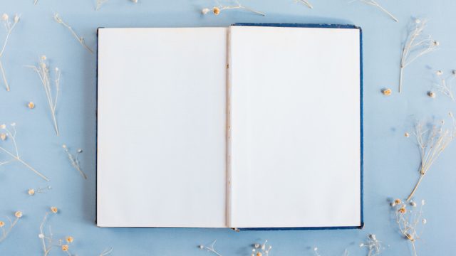 An open book on a blue table with scattered flowers around it
