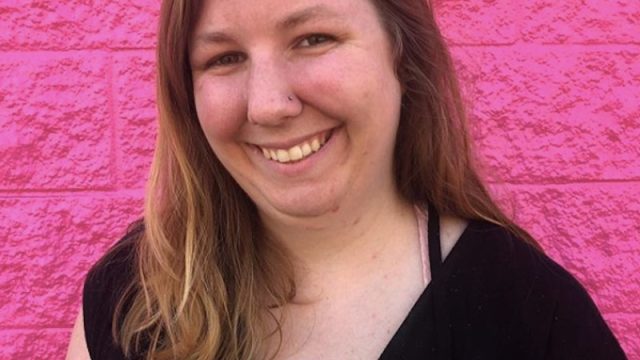 Image of the author smiling in front of a pink wall
