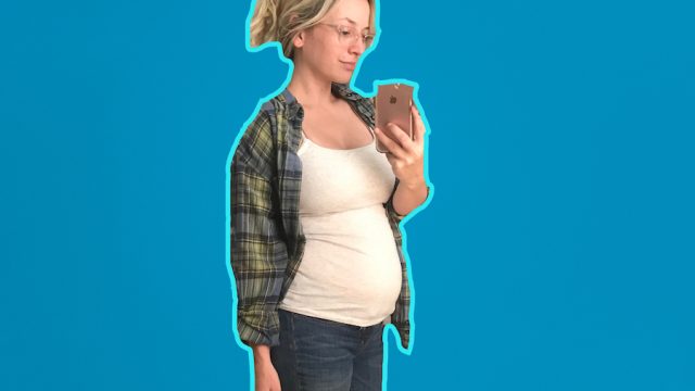 Author taking a selfie of her pregnant belly on a blue background