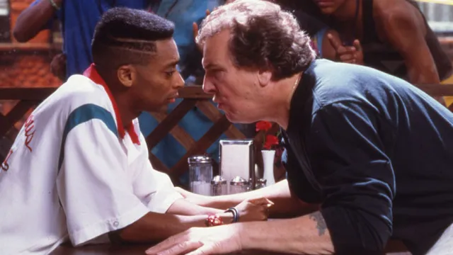 Promotional image from Spike Lee's "Dp The Right Thing" featuring Lee and actor Danny Aiello in an argument at a pizzeria as the neighborhood looks on