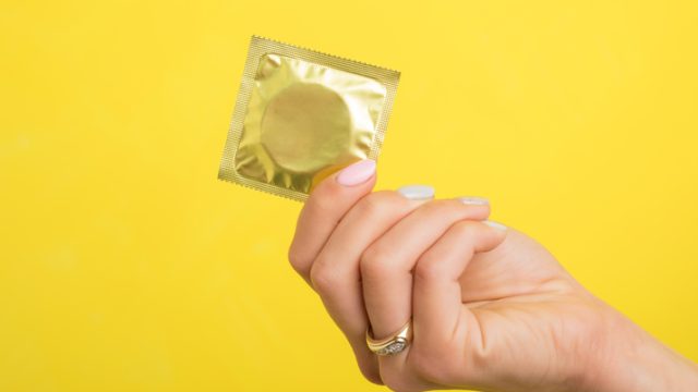 Woman's hand holding a condom in front of yellow background