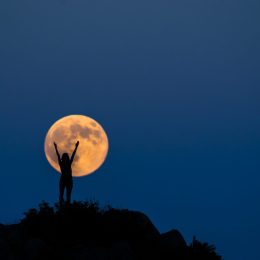 Silhouette of a woman raising her arms up in front of a full moon