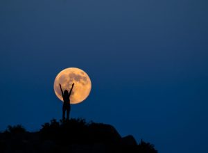 Silhouette of a woman raising her arms up in front of a full moon