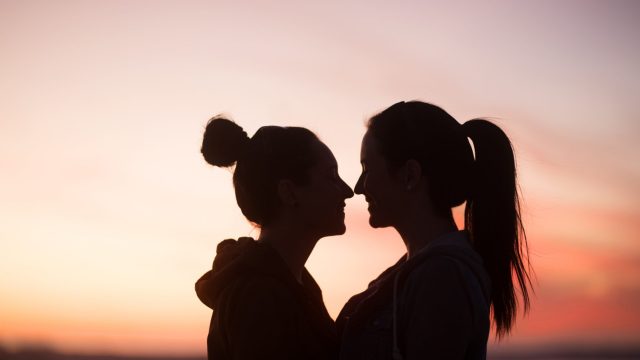 Outline of two young women standing very close to one another looking at each other at sunset
