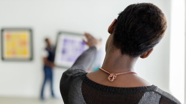 Black woman supervising art being mounted in gallery