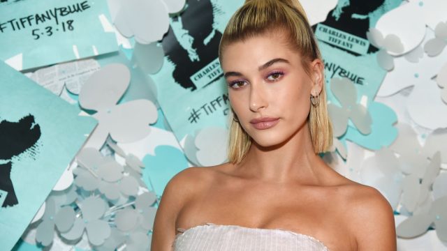 Hailey Bieber posing in front of a blue wall at the Tiffany & Co. Paper Flowers event