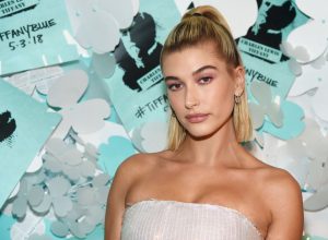 Hailey Bieber posing in front of a blue wall at the Tiffany & Co. Paper Flowers event