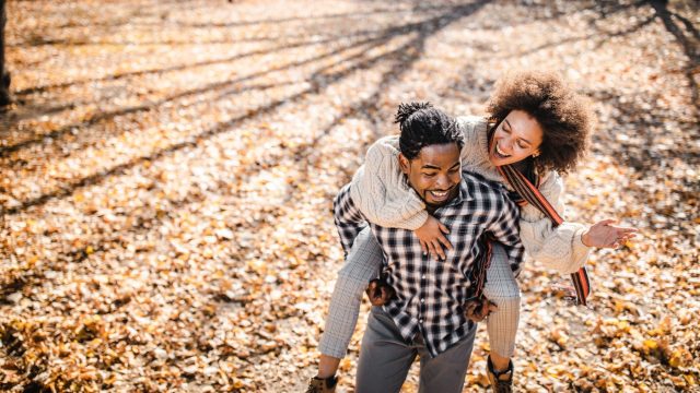 Cheerful couple piggybacking in autumn at the park