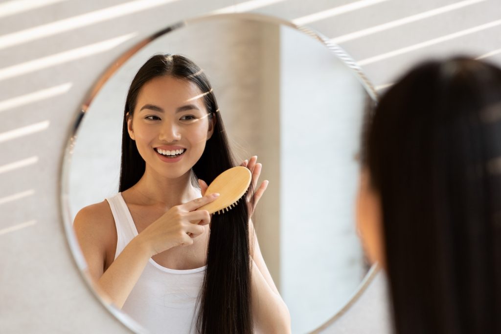 woman combing hair in mirror smiling