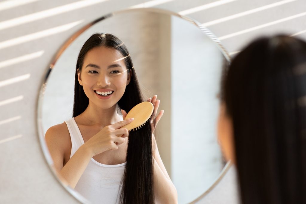 woman combing hair in mirror smiling